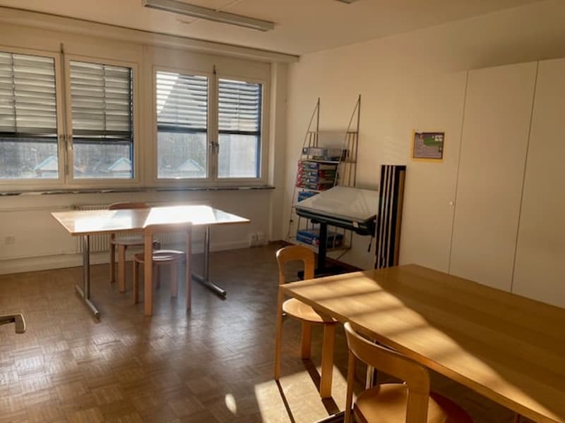 Empty room with two wooden tables, 4 chairs, windows, radiator, standing lamp, bookshelf