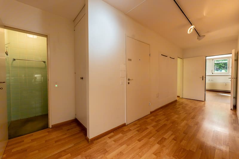 Empty room with wooden floor, white walls, two doors, one leading to a shower room, another to an open room with a window