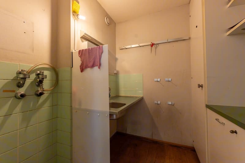 small room with sink, green tiles, wooden floor, hanging towel, power outlets, pipes