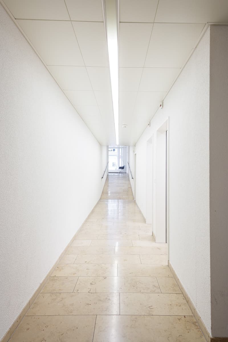 White walls, tiled floor, fluorescent ceiling light, door at the end
