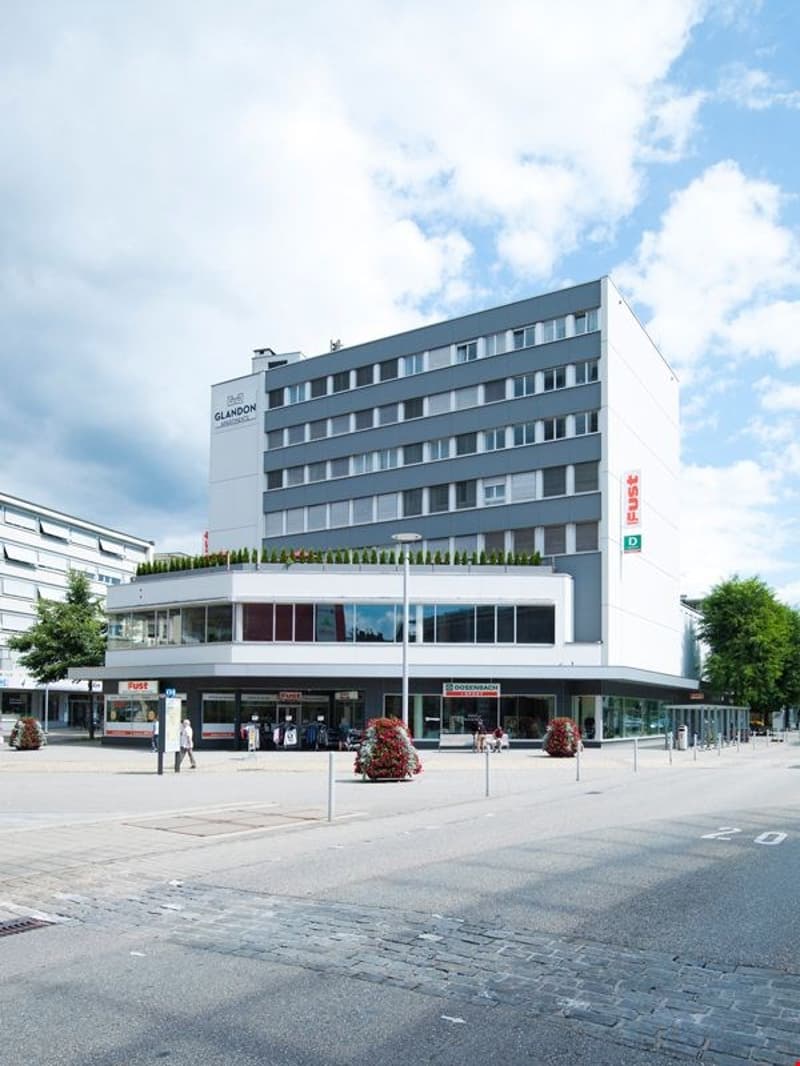 large white building with green roof, multiple floors, large windows, storefronts, large planter boxes