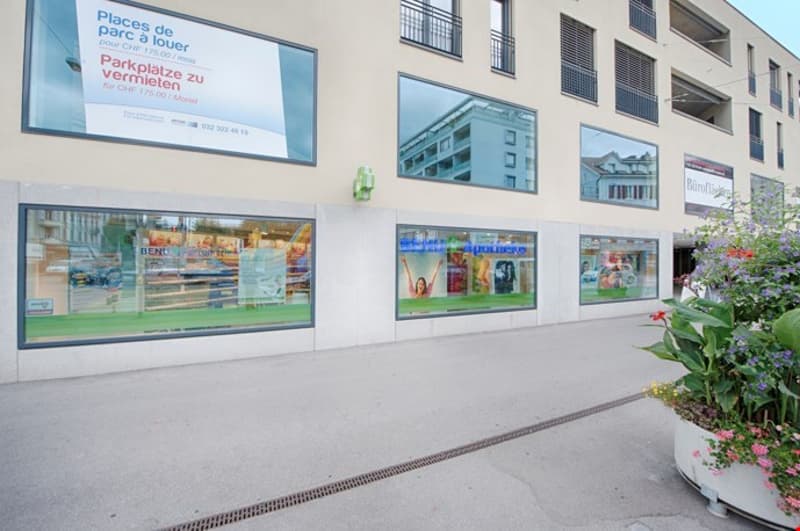 Commercial building with several glass windows, plants, and a large sign indicating parking space availability