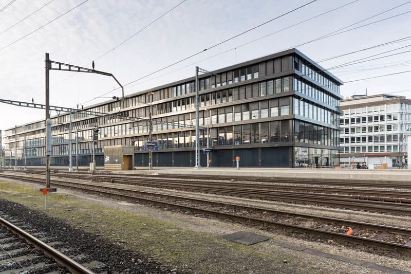 large multi-story office building, multiple windows, glass facade, multiple floors, located next to a railway track
