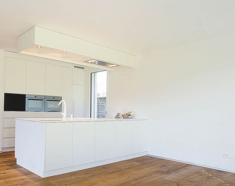 Spacious, modern kitchen with white cabinets, built-in appliances including a dishwasher, and hardwood flooring.