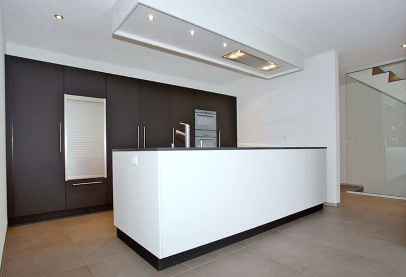 Modern kitchen with dark cabinets, white countertops, built-in appliances including a dishwasher, and recessed lighting in the ceiling.