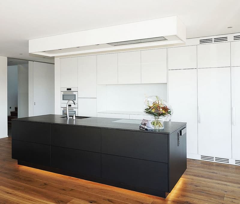 Modern kitchen with white cabinets, black island countertop, built-in appliances, and hardwood flooring.