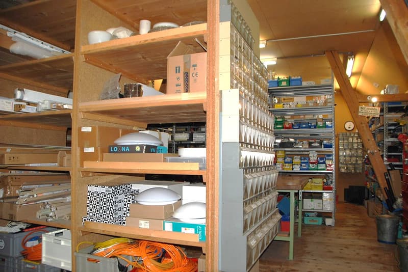 Rows of wooden shelves filled with various items, wooden floor, buckets, a ladder, a green table