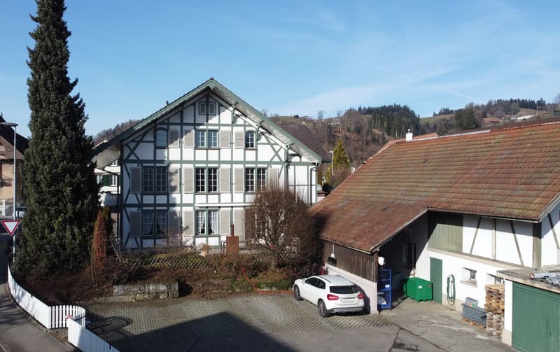 Two story house with brown roof, large garage, white car parked, stone wall, large tree