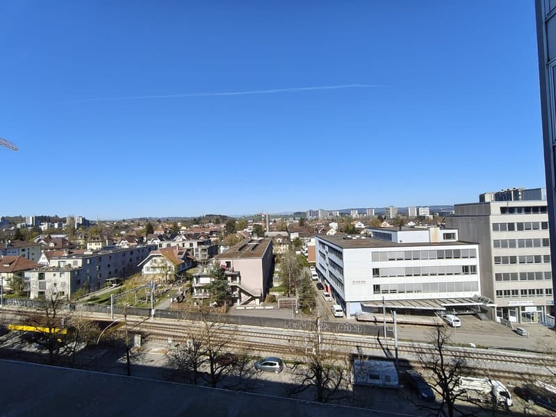 Cityscape with multiple buildings, a railway track, and a clear blue sky.