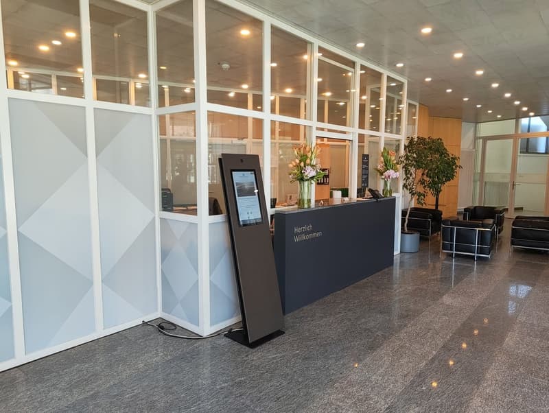 modern reception area with glass walls, black reception desk, digital screen, flowers, black chairs, gray floor