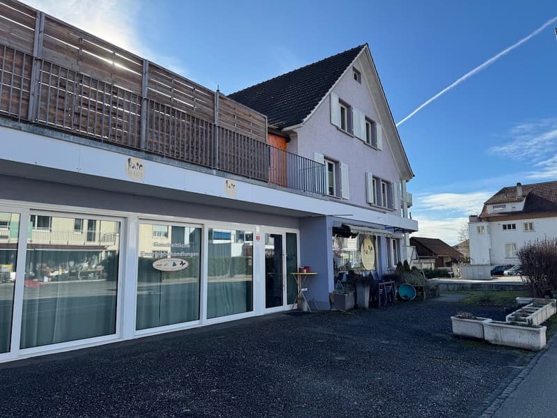 two story building, balcony on the top floor, glass walls and doors, concrete parking area