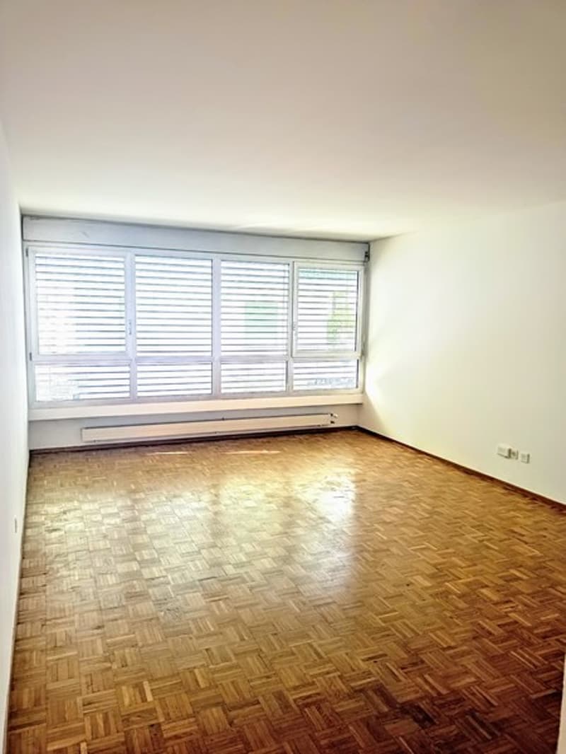 Empty room with hardwood flooring, large windows with blinds, and white walls.