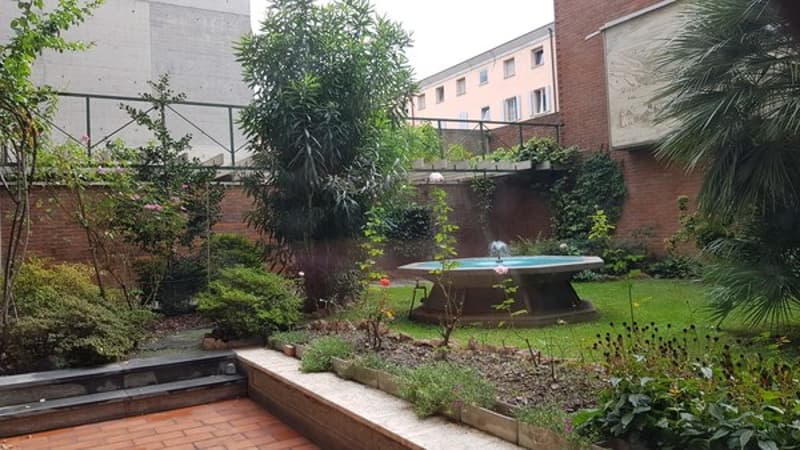 Central fountain, brick floor, manicured shrubs, pink flowers, greenery, trees