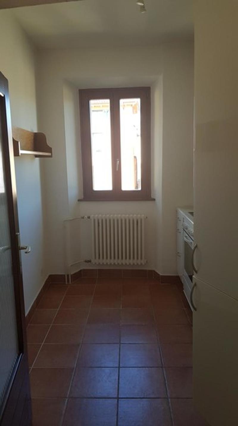 The image shows a small entryway with a tiled floor, a radiator, and a window with decorative glass panes. The walls are painted a light color, and there is a shelf or ledge on the wall.
