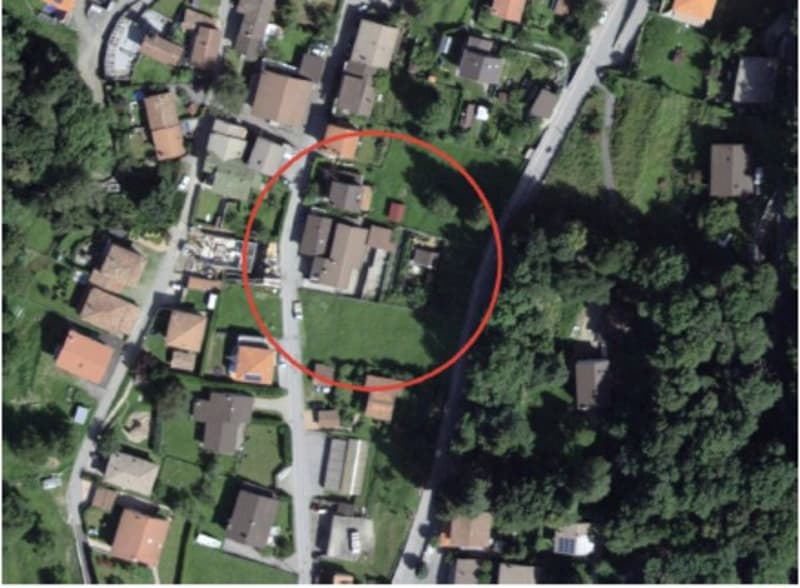 Aerial view of a residential area with houses, buildings, and green spaces. The image is circled to highlight a specific area of interest.