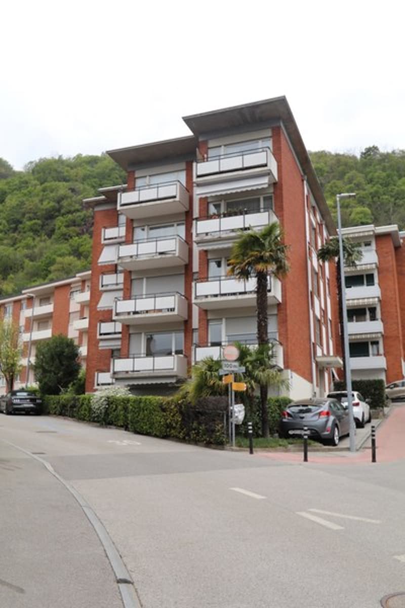 large building with multiple balconies, surrounded by trees and greenery