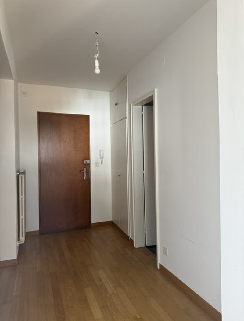 an empty hallway with wooden flooring, white walls, and a brown door