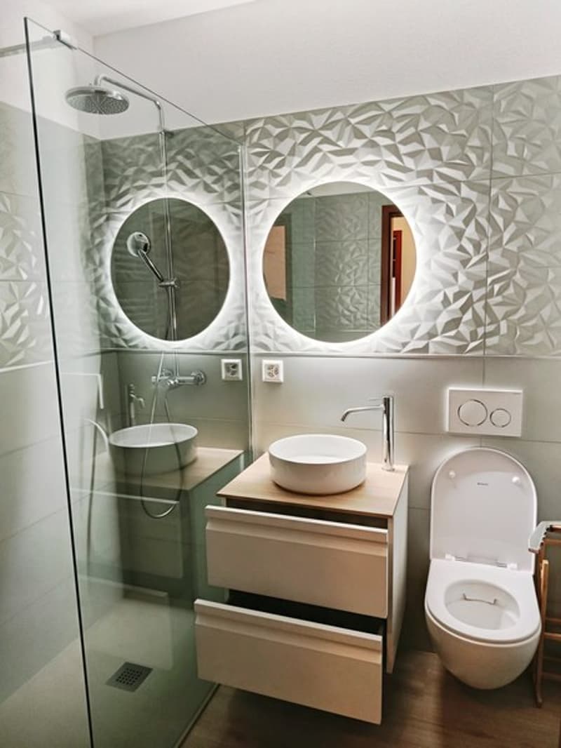 Modern bathroom with glass shower, two sinks, mirror, toilet, wooden drawers, white fixtures.