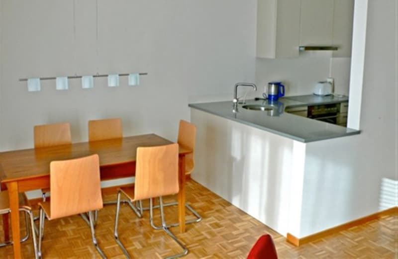 Modern kitchen area, wooden table, white wall, open kitchen, dishwasher, washing machine