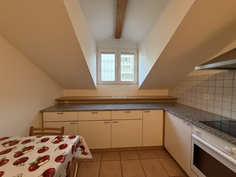 small kitchen with table, wooden chair, cabinets, white countertop, stainless steel stove and hood, granite tiled floor