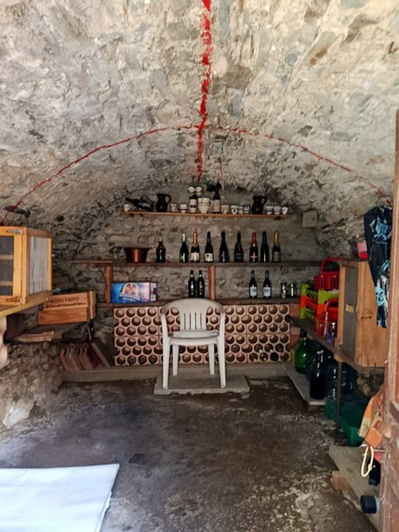 stone walls, shelves with wine bottles, white chair, wine cellar