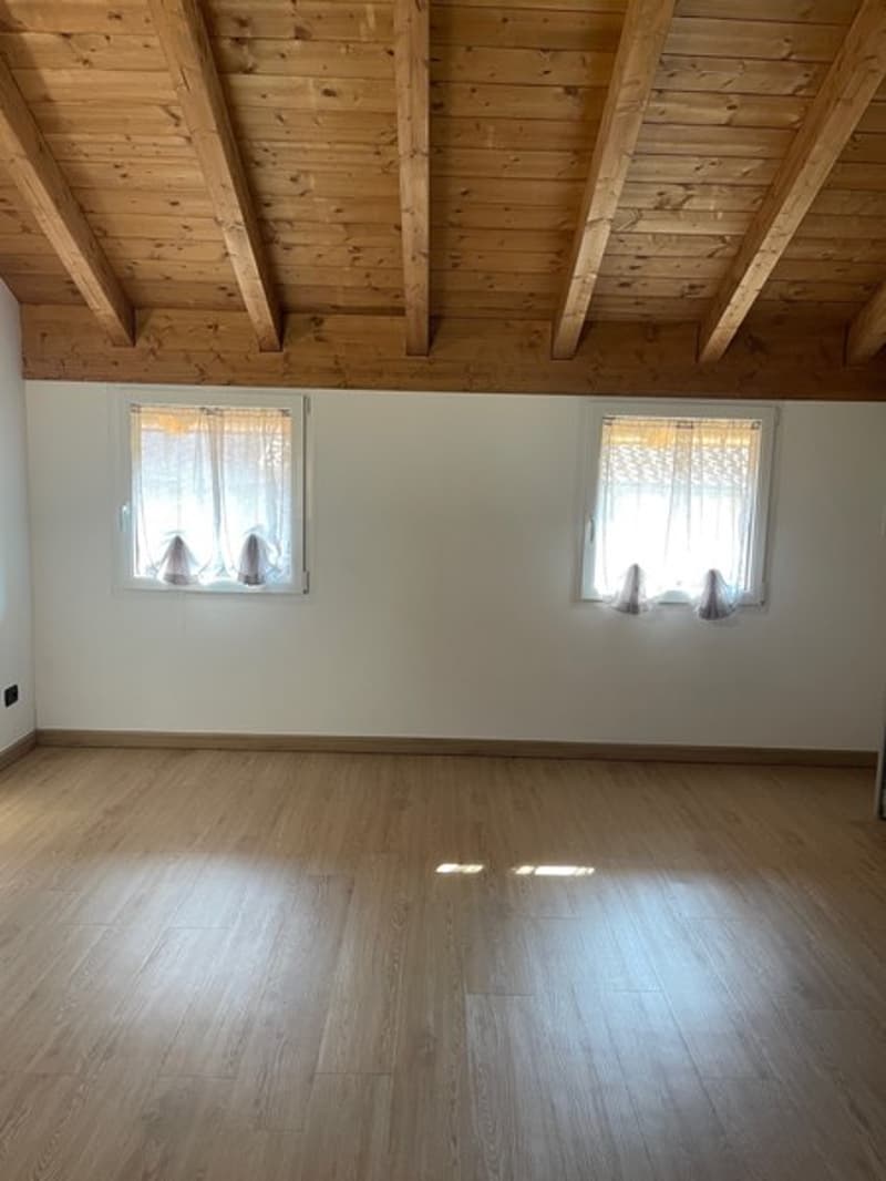 Empty room with wooden ceiling, wooden floor, white walls, and two windows with white curtains