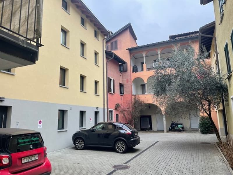 Two cars parked in a courtyard in front of a multistory building, with balconies and windows.