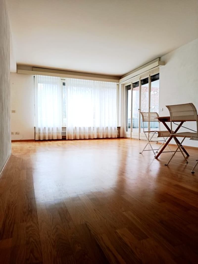 Spacious room with hardwood floors, white walls, large windows, glass doors, dining table, and chairs.