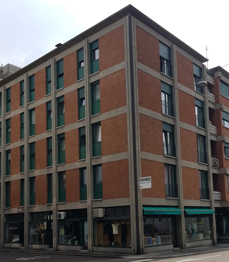 Building with 5 floors, ground floor commercial space, red brick facade, green shutters on windows, storefront sign