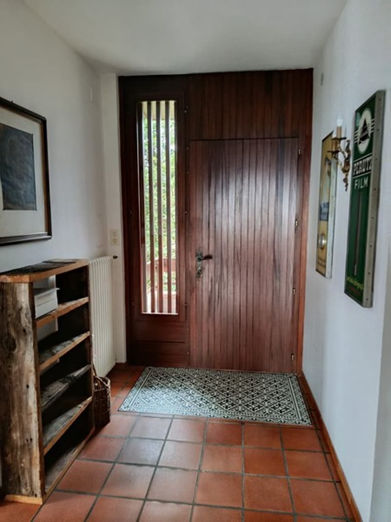 Entrance hall with wooden door, tiled floor, wooden shelf, radiator, picture frame, wall art, basket, rug