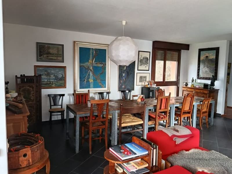 Dining room with wooden table, chairs, paintings, lamp, wooden cabinet, red couch, books, and wooden stool