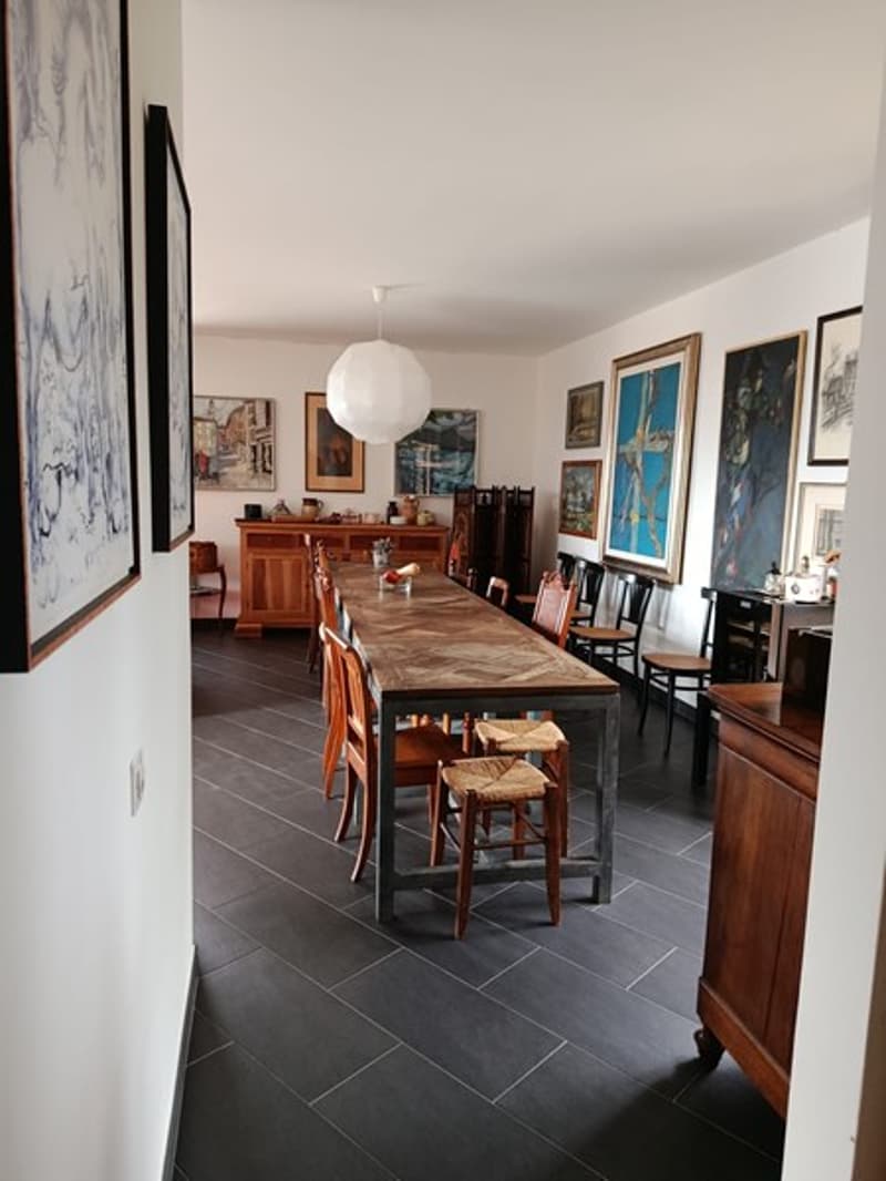 Dining room with long wooden table, wooden chairs, wooden cabinet, and several paintings on the wall