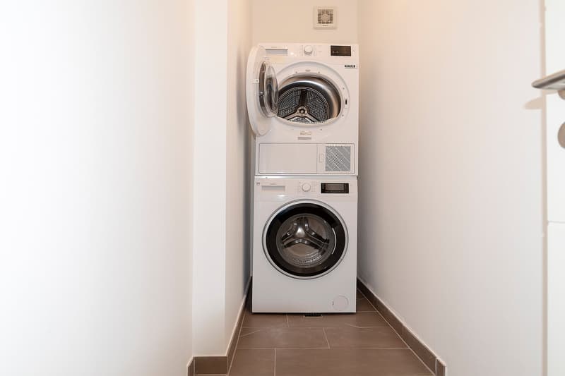 Stacked washing machine and dryer, tiled floor, white walls
