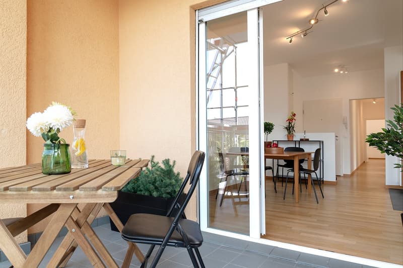 Balcony with wooden table, folding chair, plants, sliding glass door, wooden floor, dining table, chairs, plants, hallway