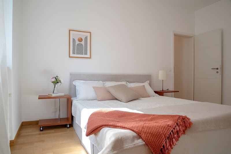 Bedroom with bed, nightstands, lamp, picture frame, flowers, and a blanket