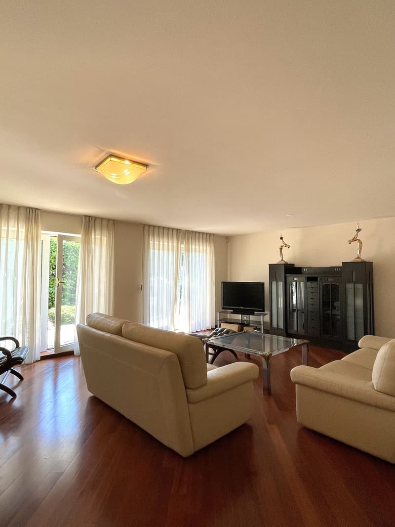 Spacious living room with beige sofas, glass coffee table, and a flat-screen TV on a stand.