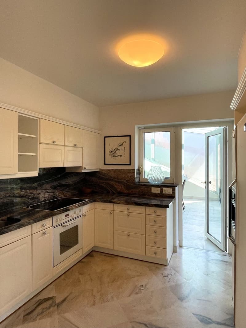 Modern kitchen with white cabinets, granite countertops, built-in oven and stove, and a ceiling light.