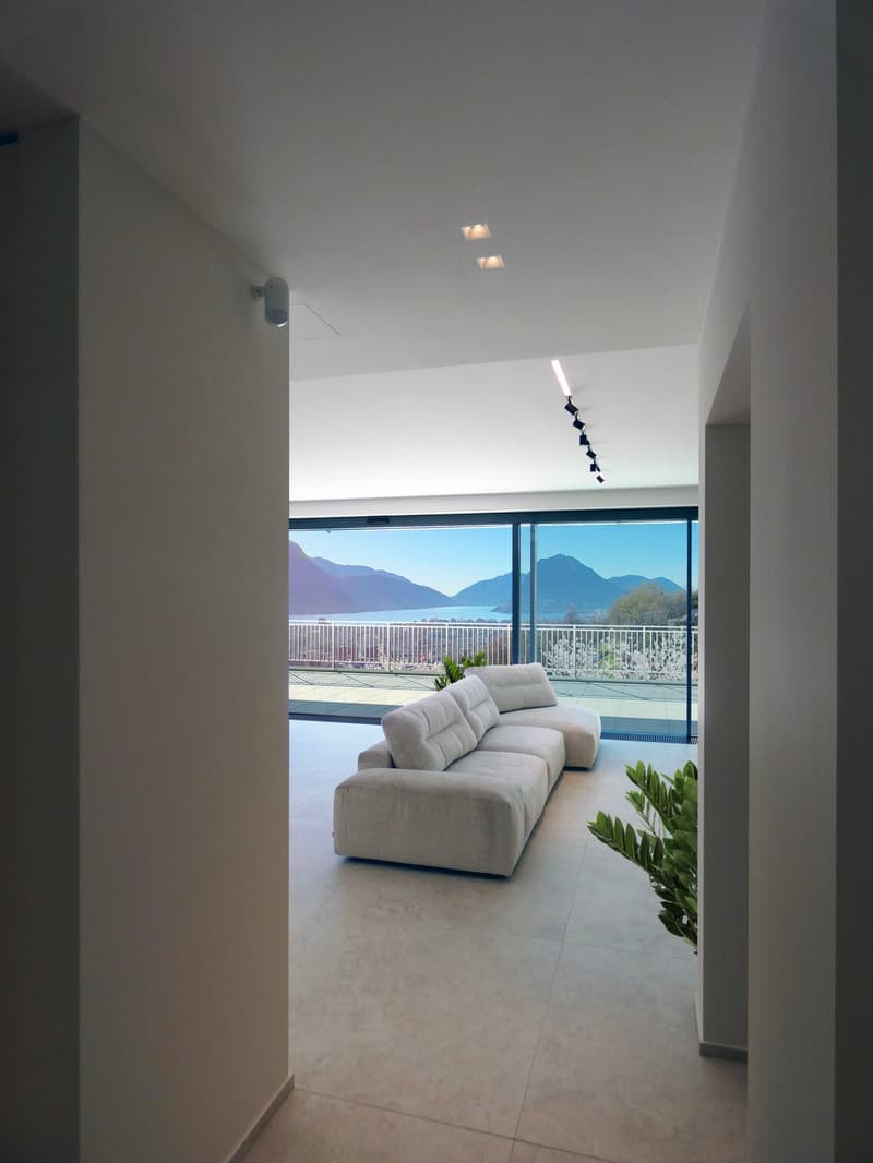 modern living room with large windows, white couch, white walls, white floor, balcony with railings, view of mountains and water
