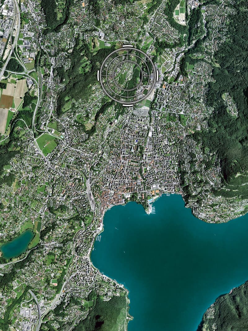 Aerial view of a city with a large lake, surrounded by green hills and mountains, with many buildings and roads