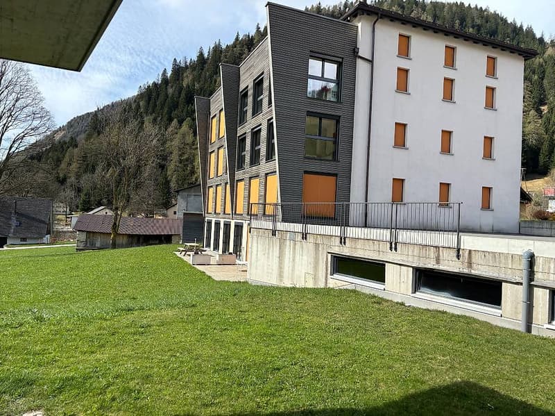 Two story building, concrete foundation, large windows, balconies, grass lawn, mountains