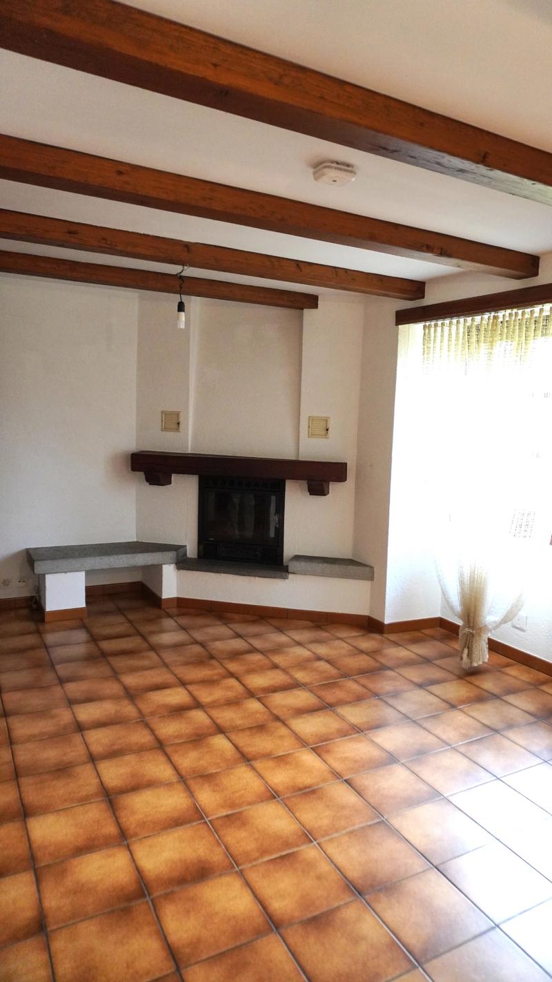Empty room with fireplace, wooden beams, tiles on the floor, power outlet, and bench by the fireplace.