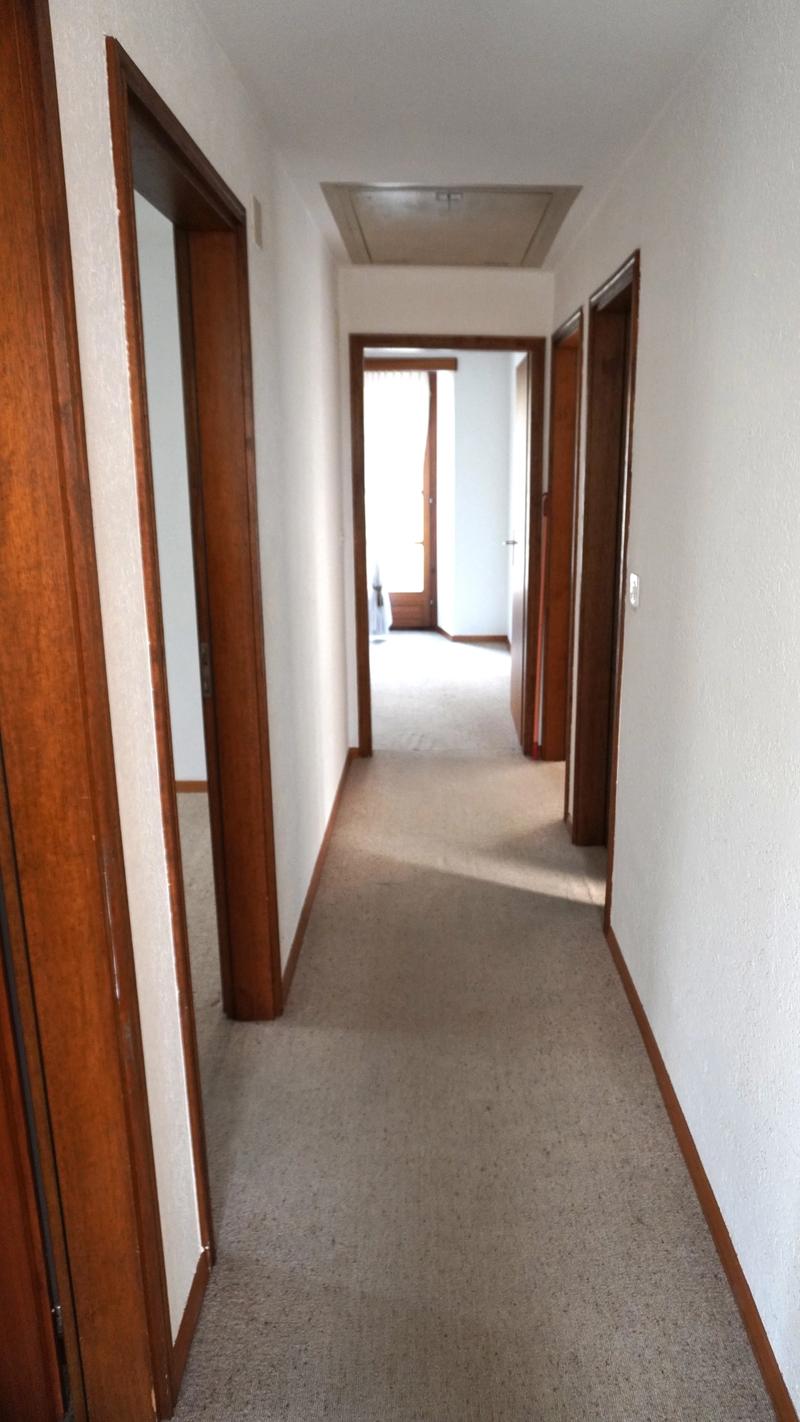 Carpeted corridor with 3 doors and a balcony
