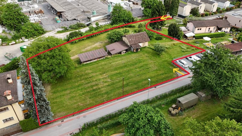 The property plot consists of two buildings with flat roofs and three detached garages. There is also an empty plot of grass. Adjacent to the plot there is a road with multiple parked cars.