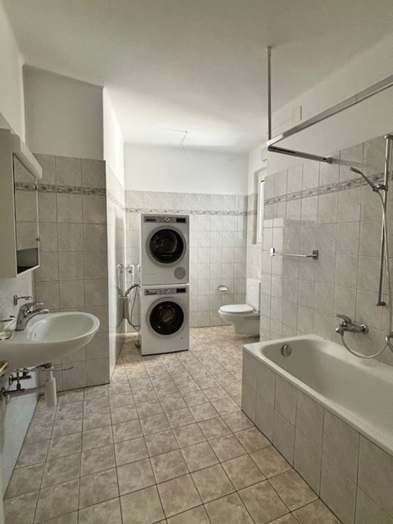 Bathroom with white tiles, bathtub, toilet, sink, washing machine, shower