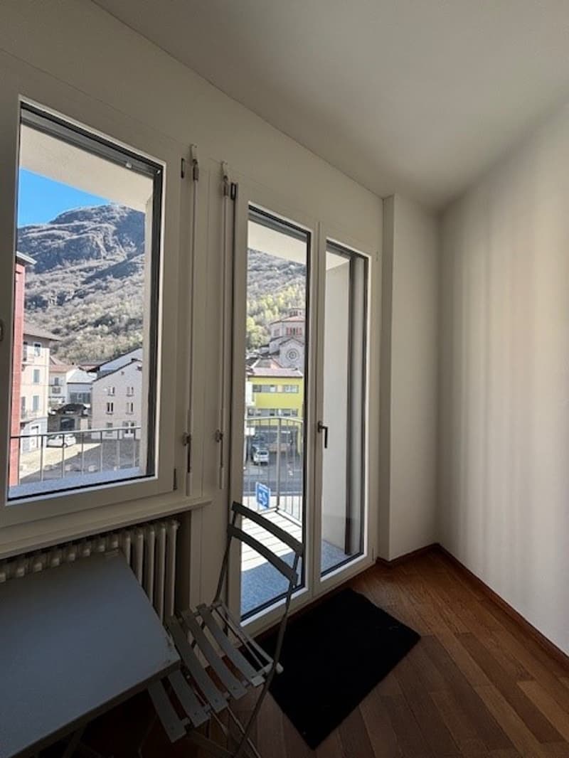 empty room, balcony, sliding glass doors, wooden floor, radiator, table, chair, black rug