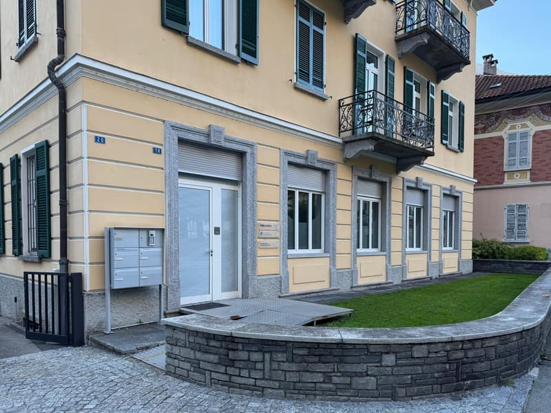 yellow building, multiple windows, balcony, mailbox, paved entrance, small garden