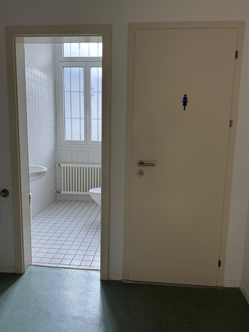 Small bathroom with white tiles, white sink, white toilet, white radiator, window