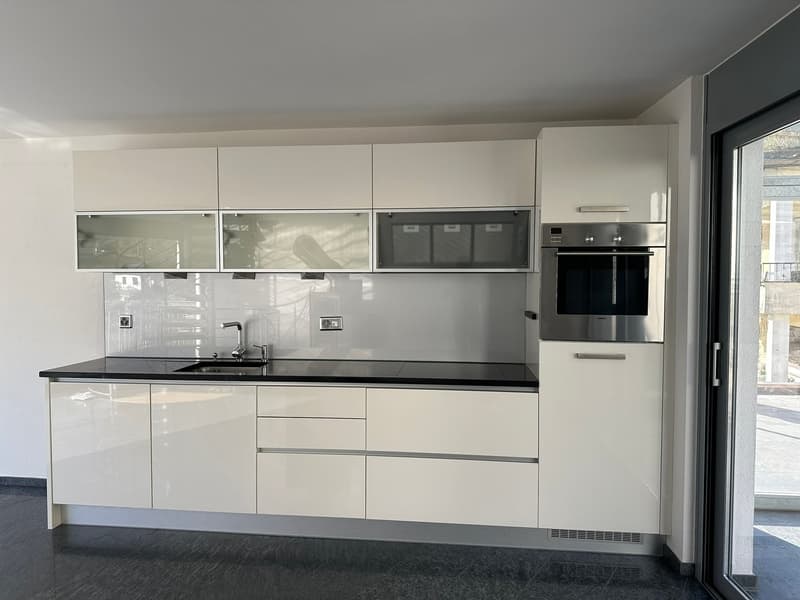 modern kitchen with white cabinets, black countertops, stainless steel oven, double sink with faucet, sliding glass door