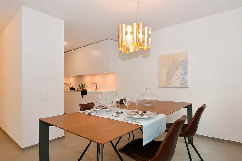 Dining table with chairs, wall painting, modern chandelier, kitchen in the background