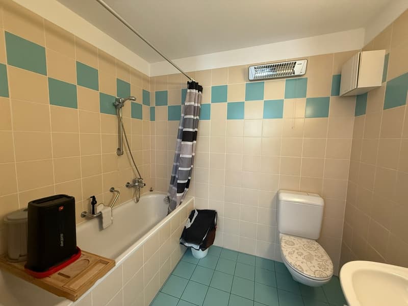 Bathroom: white bathtub, shower, toilet, sink, blue and beige tiles, trash can, towel, air conditioner